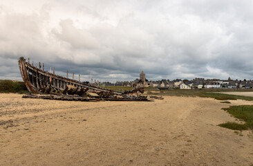 An old broken ship on the coast with residential buildings in the background under the cloudy sky