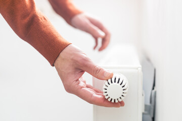 hand adjusting radiator temperature using thermostat. Home with central heating.