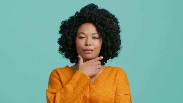 Young beautiful African American girl thoroughly thinking out an idea, holding hand at chin, fingers against cheekbone, with gesture of thought about problem solution with puzzled facial expression