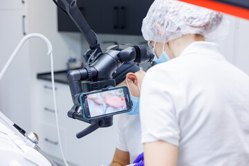 A dentist treats teeth using a dental microscope and tools. The assistant holds a syringe with air and water. Dental office