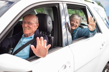 Portrait of attractive happy senior couple sitting in the car, man ready to drive, looking at camera smiling.
