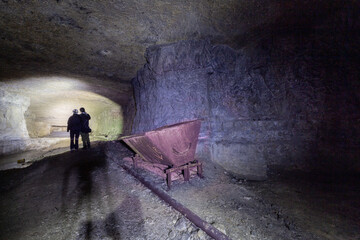 Old mine, deep underground, with an old lorry on rails. Siloette of a couple.