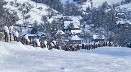 Fototapeta premium Winter rural landscape in the Carpathians. Behind the fence, on the snowy slope of the mountain, you can see a small village