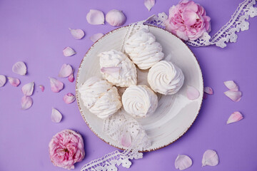Delicate aesthetic vanilla no sugar marshmallows on purple background with tea rose decorations. Healthy sweets, natural food. Valentines day present