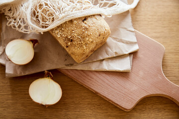 Organic sourdough unleavened onion bread on craft paper on kitchen cutting wooden board. Loaf of natural freshly baked bread. Beige rustic food background.