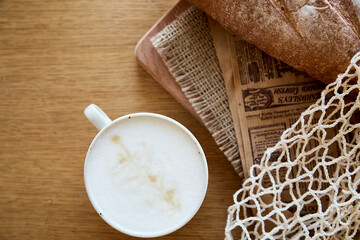 Fresh baguette, newspaper and cappuccino on wooden table in eco mesh. French breakfast