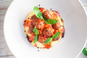 Beef meatballs in tomato sauce with mashed potatoes and basil in a white plate on a wooden background, top view