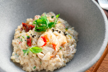Risotto with crab meat and vegetables is served in a bowl. Dish with rice and seafood close up