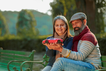 Indian old couple holding car toy in hand at park. car loan concept.