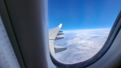 View from the window of the airplane. Rear of the wing. Blue sky, White clouds in the abackground out of focus. Selective focus. Copy space
