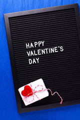 St. Valentines day postcard. Letterboard with congratulation phrase  and box with present and hearts  oh bright blue paper textured background. Top view. B