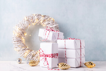 Wrapped boxes with presents,  decoraative golden cones, wreath with fairy lights  and decorative white tree on white marble against  blue textured  wall. Place for text.