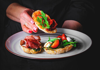 chef in a black suit holds in his hands plate with Bruschetta on Dark grey black background