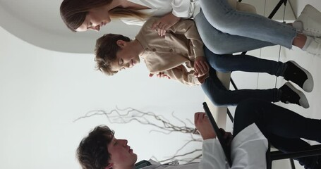 Doctor ask questions about symptoms at little boy and his mother during visit in private clinic, family get professional medical service, smile having friendly communication with reliable pediatrician