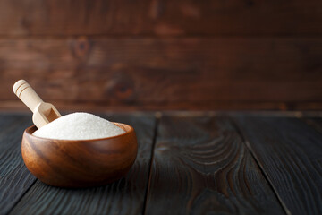 Wooden bowl with sugar on dark wooden background