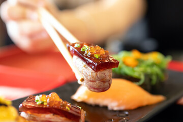 Hand holding bamboo chopsticks a piece of sushi at Japanese restaurant.