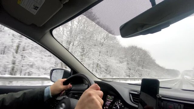 man hands on steering wheel driving car by winter highway