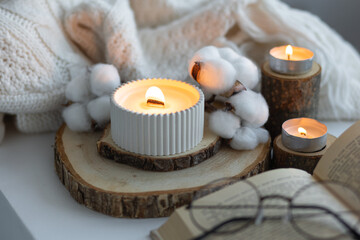 Cozy autumn or winter composition with aromatic candle, wool sweater, cotton, book. Aromatherapy, home atmosphere of cosiness and relax. Wooden background close up.