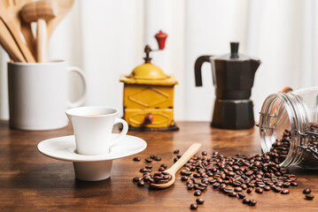 Cup of coffee on a kitchen table with a jug with wooden utensils, a coffee grinder, an Italian...