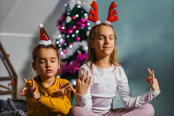 Little girls meditating on a bed in front a christmas tree, they are copying their mum and having fun