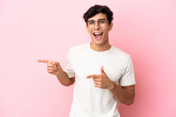 Young Argentinian man isolated on pink background surprised and pointing side