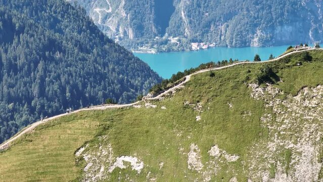 Hiker hikers on a mountain ridge trail in Switzerland, swiss alps mountains. Recreational summer leisure activity. Green alps and grass. Aerial drone overhead.