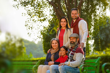 happy Indian family sitting at park in winter wear or warm clothes