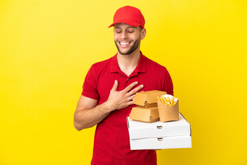 pizza delivery man picking up pizza boxes and burgers over isolated background smiling a lot