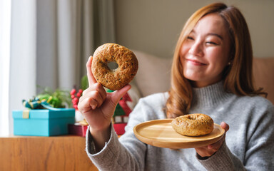 Portrait image of a young woman in sweater holding a plate of bagel with Christmas holiday...