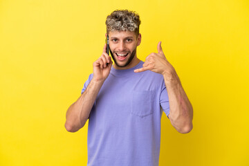 Young caucasian man using mobile phone isolated on yellow background making phone gesture. Call me back sign