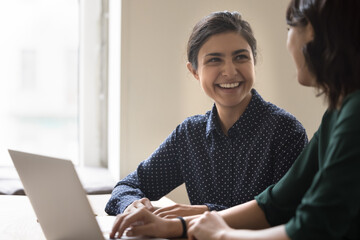 Happy young Indian employee woman talking to colleague, smiling, laughing, discussing career...