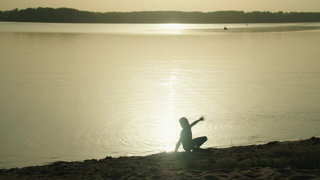 Cheerful, athletic boy does a gymnastic wheel on the ocean shore, the silhouette of a running wild at sunset