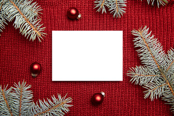 Christmas greeting card mockup, fir tree branches and holiday decorations on red knitted sweater background, top view, flat lay. Blank New Year card with winter decor