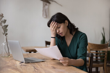 Upset exhausted freelance employee woman getting job report with mistake, holding paper document at work table with laptop, touching head with closed eyes, doing boring paperwork