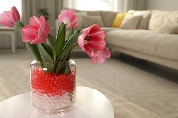 Obraz na płótnie Canvas Different color fillers and tulips in glass vase on white table at home, space for text. Water beads