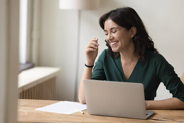 Happy Asian millennial employee woman in casual having fun at workplace table, laughing at laptop computer, enjoying work on business project, job tasks, online communication