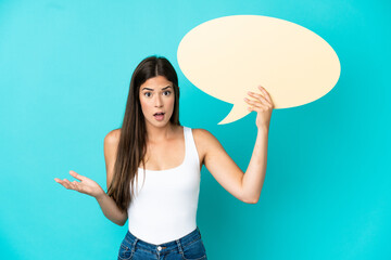 Young Brazilian woman isolated on blue background holding an empty speech bubble with surprised expression