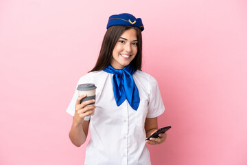 Airplane stewardess Brazilian woman isolated on pink background holding coffee to take away and a mobile