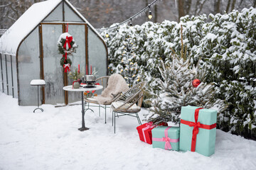 Beautifully decorated backyard with gift boxes, christmas tree and wreaths on winter holidays at snowy backyard