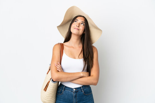 Young Brazilian woman with Pamela holding a beach bag isolated on white background looking up while smiling