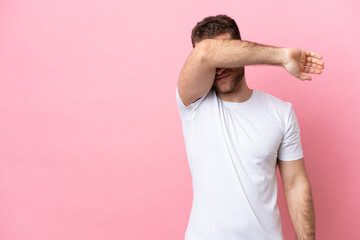 Young caucasian man isolated on pink background covering eyes by hands