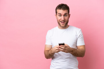 Young caucasian man isolated on pink background surprised and sending a message