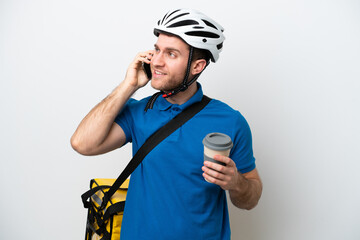 Young caucasian man with thermal backpack isolated on white background holding coffee to take away and a mobile