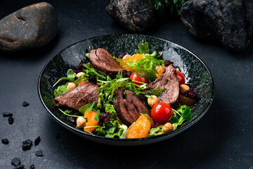 Salad beef steaks, lettuce, arugula, tomatoes, tangerines and hazelnuts on a dark table.
