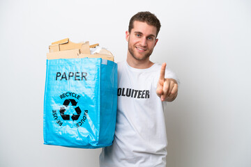 Young caucasian man holding a recycling bag full of paper to recycle isolated on white background showing and lifting a finger