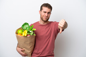 Young caucasian man holding a grocery shopping bag isolated on white background showing thumb down...
