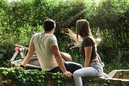 Couple making a selfie. Couple on the road sitting taking a selfie with their mobile as a souvenir. Young beautiful couple of tourists take a selfie in a place with nature in the city. People photo