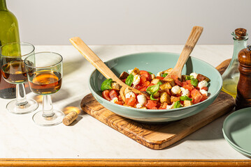 Classic italian panzanell salad with tomatoes, basil, bread, mozzarella on white kitchen table. Served with wine. Overhead view.