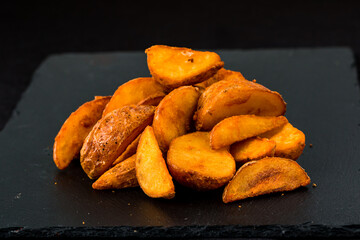 A heap of fried potato slices on a dark slate board.