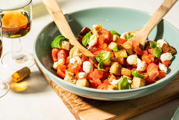 Classic italian panzanell salad with tomatoes, basil, bread, mozzarella on white kitchen table. Served with wine. Overhead view.